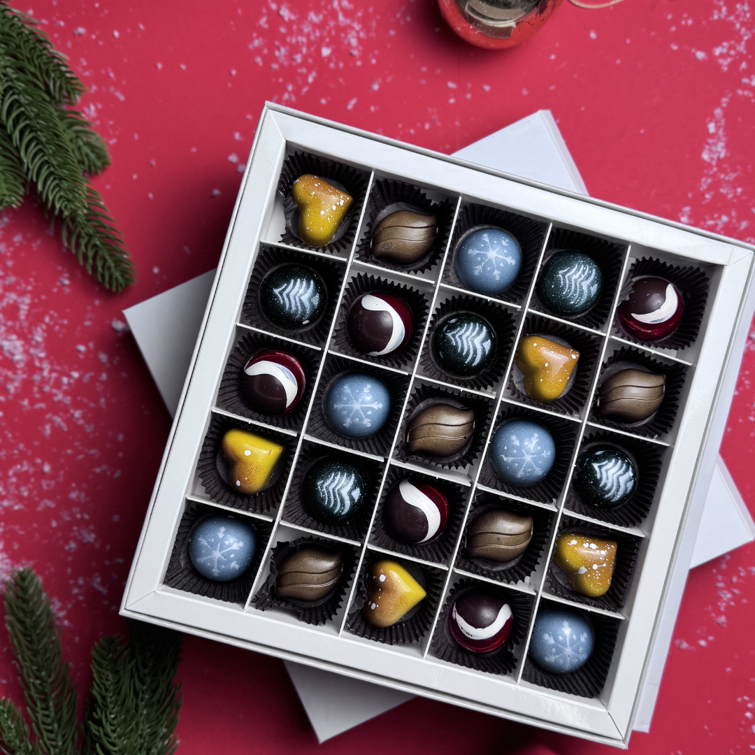 Box of assorted chocolates on a red surface with Christmas decorations.
